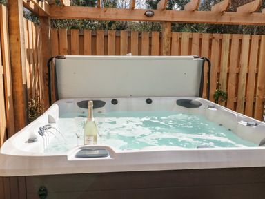 An outdoor hot tub with bubbling water glasses and a bottle of champagne surrounded by wooden fencing at Gloccamaura in Bovey Tracey