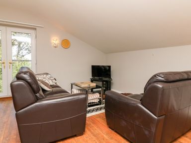 A living room with two brown leather sofas a glass coffee table and a television at Hazelwood Lodge in High Bickington