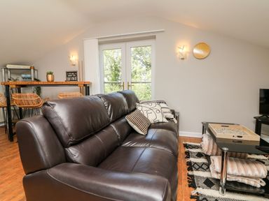 A living room with a brown leather sofa soft cushions a glass coffee table with a tray and throws a wooden floor near a dining area with wicker chairs and double doors at Hazelwood Lodge in High Bickington