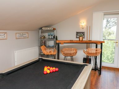 A games room with a pool table and three wicker stools at a high table by a glass door at Hazelwood Lodge in High Bickington