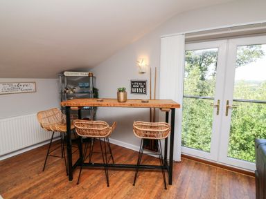 A wooden tall table with three wicker stools near a glass door with trees outside at Hazelwood Lodge in High Bickington