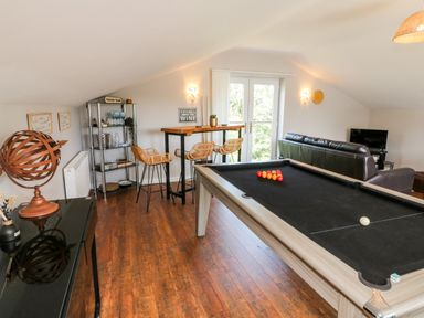 A game room with a pool table, bar stools, a sofa, and glass doors at Hazelwood Lodge in High Bickington