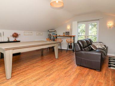 A room with a pool table a brown leather sofa bar stools and double doors at Hazelwood Lodge in High Bickington