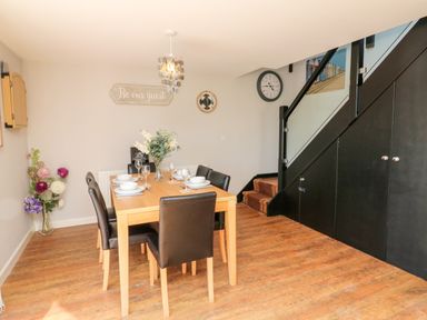 A dining room with a wooden table and six chairs near stairs with black storage at Hazelwood Lodge High Bickington