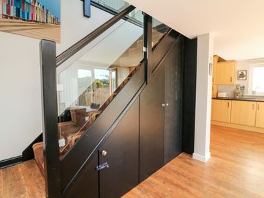 A staircase with black paneling and glass railing next to a kitchen with wooden cabinets