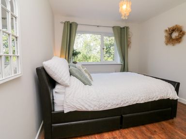 A bedroom with a double bed near a window with green curtains and a mirror on the wall at Hazelwood Lodge in High Bickington