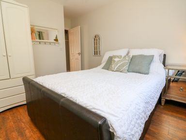 A bedroom with a bed white bedding pillows a white wardrobe wooden floor and a mirror at Hazelwood Lodge in High Bickington