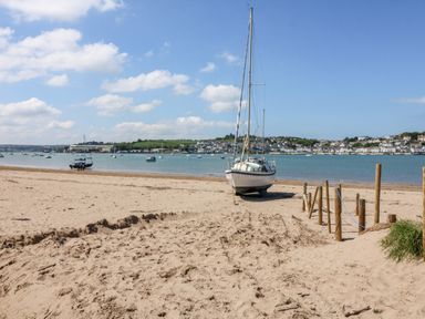 A sailboat on a sandy beach near wooden posts with water and houses in the background at Hazelwood Lodge in High Bickington
