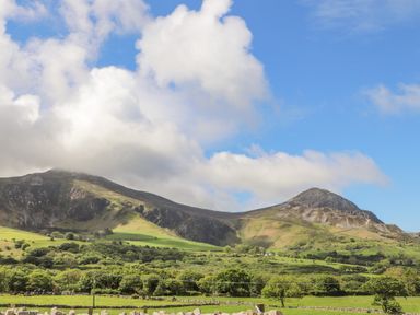 A landscape with green fields trees and mountains under a partly cloudy sky at Caban Cwtch The Cosy Cabin in Llanaelhaearn