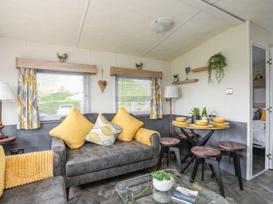A living room with gray sofas and yellow cushions a glass coffee table and a dining table with four stools at Caban Cwtch The Cosy Cabin in Llanaelhaearn