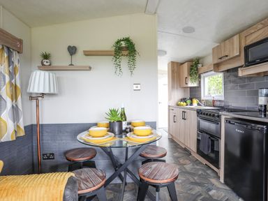 A kitchen and dining area with a glass table set for four and wooden cabinets at Caban Cwtch The Cosy Cabin in Llanaelhaearn