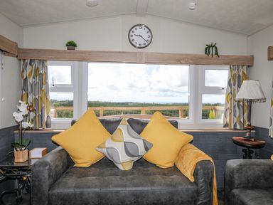 A living room with a gray sofa with yellow and patterned cushions and a window with curtains at Caban Cwtch The Cosy Cabin in Llanaelhaearn