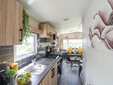 A kitchen with wooden cabinets and a sink next to a living area with a sofa and coffee table at Caban Cwtch The Cosy Cabin in Llanaelhaearn