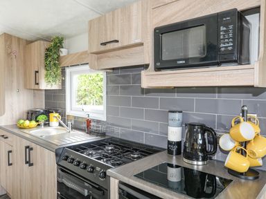 A kitchen with a gas stove sink microwave kettle and yellow mugs at Caban Cwtch The Cosy Cabin in Llanaelhaearn