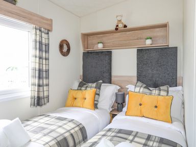 A bedroom with two single beds with plaid bedding and yellow cushions at Caban Cwtch The Cosy Cabin in Llanaelhaearn