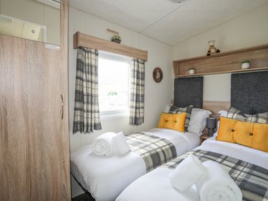 A bedroom with two single beds with checkered bedding and yellow cushions at Caban Cwtch The Cosy Cabin in Llanaelhaearn
