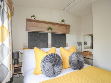 A bedroom with a bed with yellow and gray pillows a wooden shelf with small plants and a small desk with a mirror at Caban Cwtch The Cosy Cabin in Llanaelhaearn