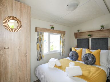 A bedroom with a bed with yellow and gray pillows and blankets near a window with patterned curtains at Caban Cwtch The Cosy Cabin in Llanaelhaearn