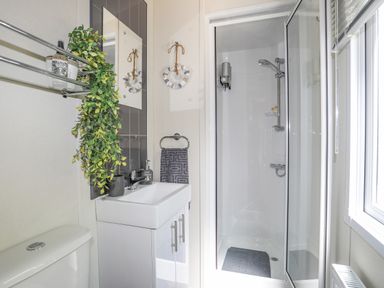 A bathroom with a shower cubicle sink with cabinet and mirror over it a towel ring with towel and a hanging wreath at Caban Cwtch The Cosy Cabin in Llanaelhaearn