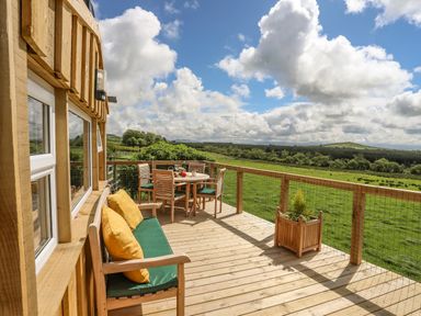 A wooden deck with a bench and table set overlooking green fields at Caban Cwtch (The Cosy Cabin) in Llanaelhaearn