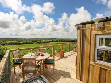 A wooden deck with a round table and four chairs overlooking green fields at Caban Cwtch The Cosy Cabin in Llanaelhaearn