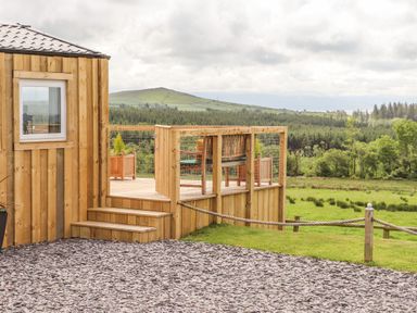 A wooden deck with chairs overlooking a field and hills at Caban Cwtch in Llanaelhaearn