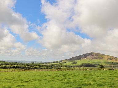 A grassy field with a fence and a hill in the background under a partly cloudy sky at Caban Cwtch The Cosy Cabin in Llanaelhaearn