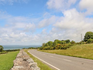 A winding road with a stone wall on one side and greenery on the other overlooking water at Caban Cwtch The Cosy Cabin in Llanaelhaearn