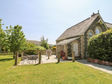 A stone house with a slate roof and a small patio area with chairs and a table surrounded by a garden at St Marks School House Nant-Glas near Rhayader