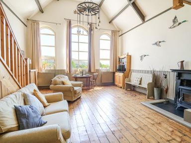 A living room with wooden floors a sofa armchair dining table bookshelf and a fireplace at St Marks School House in Nant-Glas near Rhayader