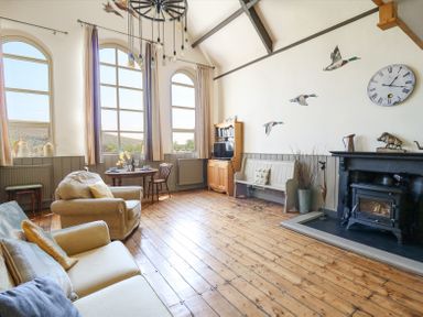 A sitting room with sofas a round table a wooden bench a fireplace and wall clock at St  Marks School House in Nant-Glas near Rhayader