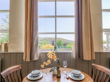 A dining table set for two with plates bowls wine glasses and a bottle in front of a window with curtains at St Marks School House in Nant-Glas near Rhayader