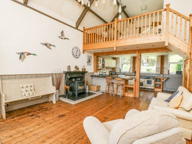 A living room with wooden floor beams a wood burning stove and an open kitchen at St Marks School House Nant-Glas near Rhayader