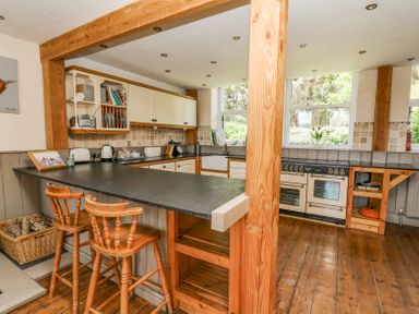 A kitchen with wooden bar stools black countertop wooden floor and white cabinets at St Marks School House Nant-Glas near Rhayader