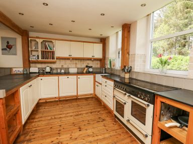 A kitchen with wooden cabinets black countertops a stove and a window with flowers at St Marks School House in Nant-Glas near Rhayader