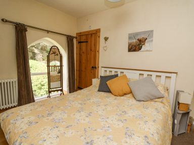 A bedroom with a bed with floral bedding pillows a wooden door a standing mirror and a painting of a bull at St Marks School House in Nant-Glas near Rhayader