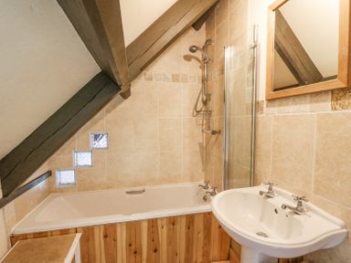 A bathroom with a bathtub next to a sink under a slanted ceiling with wooden beams at St Marks School House Nant-Glas near Rhayader