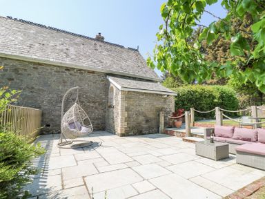 An outdoor patio area with a wicker hanging chair and a seating area with a sofa and table in front of a stone building at St Marks School House Nant-Glas near Rhayader