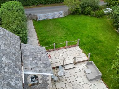 A patio with table and chairs and a lawn surrounded by plants and a white gate at St Marks School House in Nant Glas near Rhayader