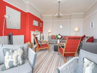 A living room with red accent wall sofas armchairs and a fireplace at Llys Owen in Criccieth