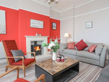 A living room with a fireplace grey sofa red armchairs and a wooden coffee table at Llys Owen in Criccieth