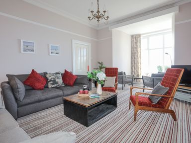 A living room with gray sofa red chairs coffee table and striped carpet at Llys Owen in Criccieth