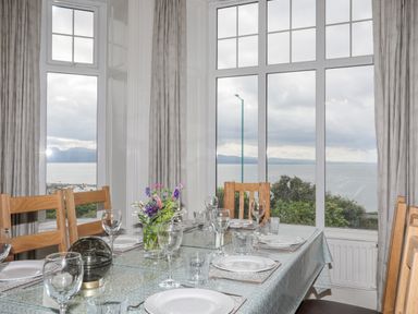 A dining room with a table set for six and large windows showing a sea view at Llys Owen in Criccieth