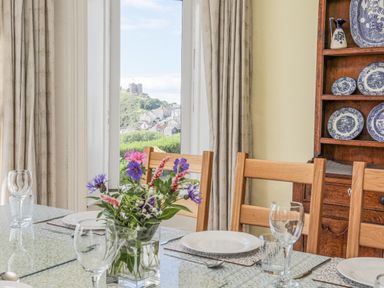 A dining table set with plates and glasses near a window showing a castle on a hill at Llys Owen in Criccieth