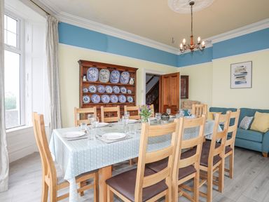 A dining room with a table set for eight people and a wooden cabinet with blue and white plates on display at Llys Owen in Criccieth