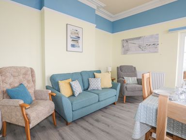 A sitting room with armchairs a sofa cushions a dining table and wall art at Llys Owen in Criccieth