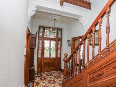 A hallway with wooden staircase stained glass door and patterned tile floor at Llys Owen in Criccieth