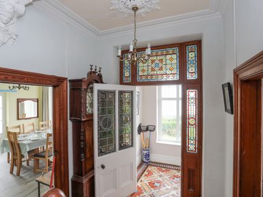 An entrance hallway with stained glass panels on the door and windows a grandfather clock and a dining room visible through an open door at Llys Owen in Criccieth