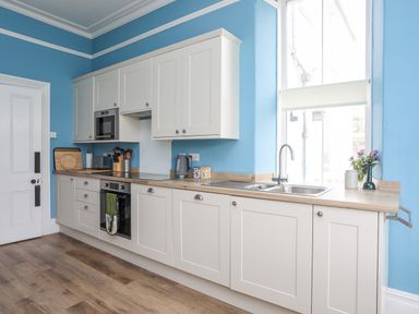 A kitchen with white cabinets wooden countertops a sink and a window at Llys Owen in Criccieth