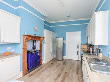A kitchen with blue walls white cabinets a blue stove a stainless steel refrigerator and a wooden floor at Llys Owen in Criccieth